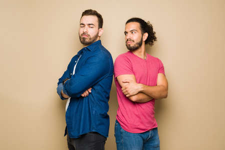 Angry gay couple looking upset and ignoring each other after a fight because of relationship problemsの写真素材