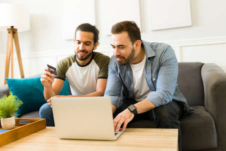 Mixed-race attractive couple paying for their online shopping with a credit card while relaxing in the living roomの写真素材