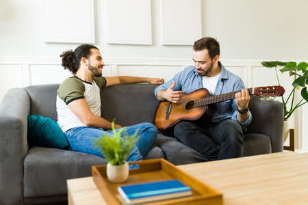 Talented young man playing the guitar and singing a romantic song to his boyfriend while hanging out...