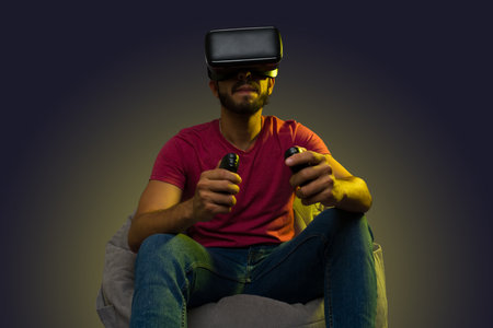 Attractive latin man using immersive technology playing a virtual reality videogame on a comfy bean bagの写真素材