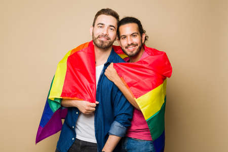 Portrait of an attractive queer couple using a rainbow flag while hugging and supporting the gay LGBT communityの写真素材