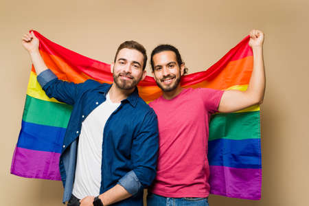 Confident gay multiracial men looking happy holding a rainbow flag to support LGBT rights in front of a studio backgroundの写真素材