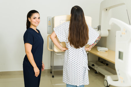 Happy female technician smiling while helping a young woman get a chest x-ray at the medical imaging labの写真素材