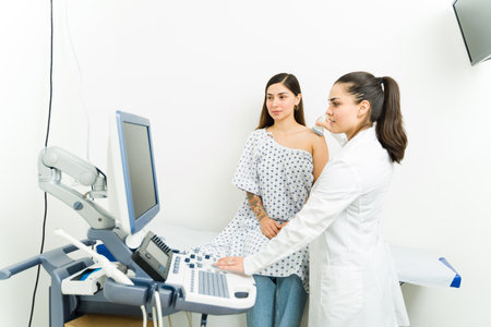 Beautiful latin woman with a female doctor getting a sonography scan medical exam to check her arm and shoulderの写真素材