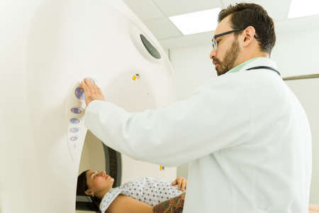 Caucasian male radiologist seen from behind starting the machine to do a CAT scan or tomography on a...