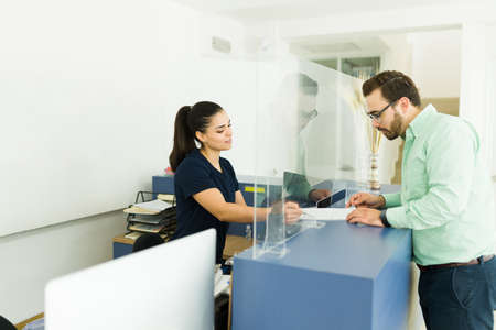Radiologist technician giving a release paper to sign to a caucasian young man before doing his medical exams at the imaging laboratoryの写真素材