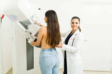 Happy female doctor or radiologist on a lab coat smiling while helping a young woman during a mammogram medical examの写真素材