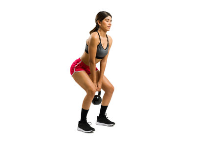 Attractive hispanic woman working out lifting a heavy kettlebell weight while doing squat exercises