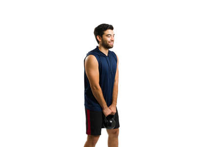 Cheerful handsome man enjoying lifting weights and exercising with cross training while holding a kettlebell weightの写真素材
