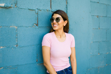 Attractive happy woman with sunglasses smiling enjoying a summer day outdoors standing in front of a...