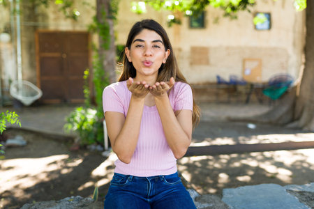 Lovely young woman blowing a kiss looking at the camera and feeling in love and romantic while relaxing outdoorsの写真素材