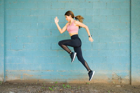 Full length of an active fit woman running and jumping during her workout outdoors in front of a...