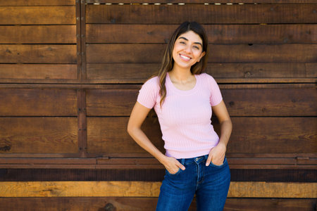 Young woman smiling looking gorgeous while posing in front of a wooden door wall outdoorsの写真素材