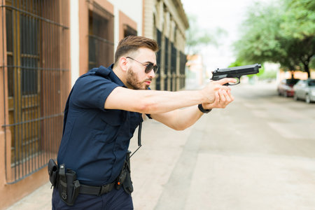Profile of a caucasian police agent pointing his gun to a criminal suspect trying to do an arrest in the streetの写真素材