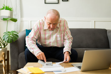 Elderly senior caucasian man at home calculating his pension while doing his taxes and monthly...