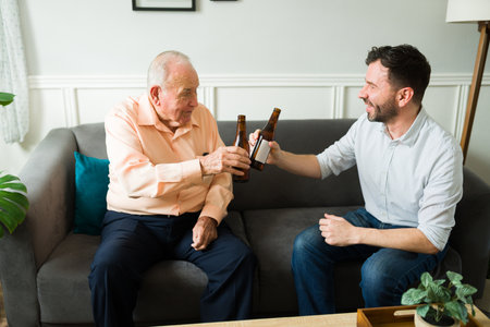 Happy senior man and young man toasting drinking beer while celebrating with family at homeの写真素材