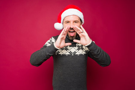 Excited young man with a santa hat screaming with happiness and giving a happy holiday messageの写真素材
