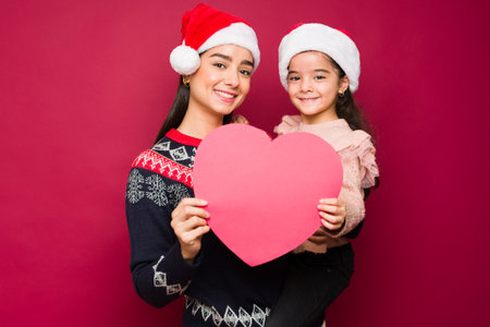 Mother and little girl smiling and sharing love while holding a red heart during the christmas holidaysの写真素材