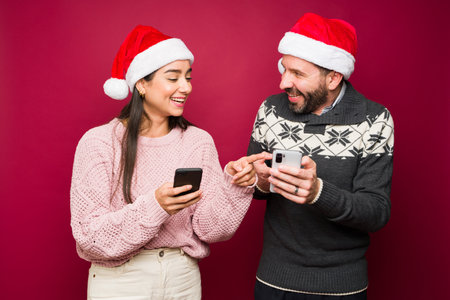 Cheerful couple laughing while texting family and friends for the christmas holidays and using...