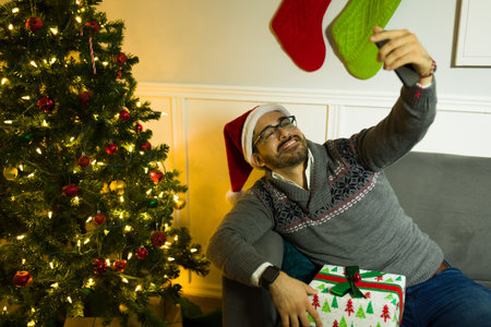 Cheerful caucasian man smiling while taking a selfie next to the tree with a smartphone after...
