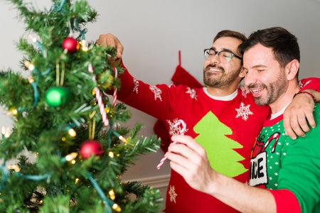 Cheerful gay couple laughing while putting candy canes on their christmas tree while huggingの写真素材