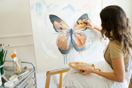 Young female painter seen from behind using a palette and her finger to paint a beautiful butterfly on an art canvasの写真素材