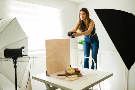 Attractive food photographer standing on a chair to take a high angle photo at the professional...