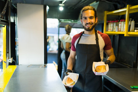 Latin male chef smiling looking happy while finishing preparing fast food at the food truckの写真素材