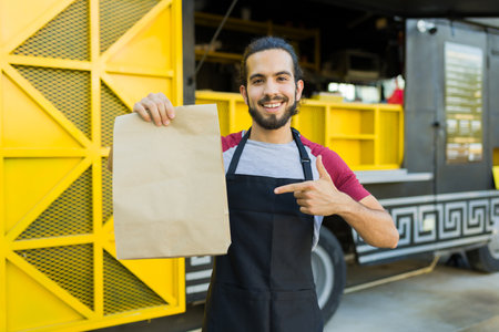 Happy latin chef pointing to a mock-up bag ready for customer delivery from the fast food truckの写真素材