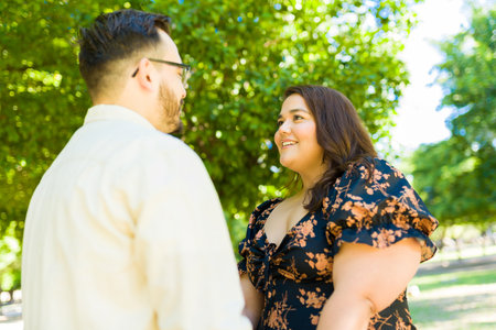 Cheerful beautiful fat woman smiling while looking at her boyfriend while holding hands during a date outdoorsの写真素材