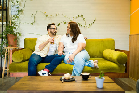 Fun happy couple sitting on the sofa on a beautiful coffee shop while drinking coffee on a dateの写真素材