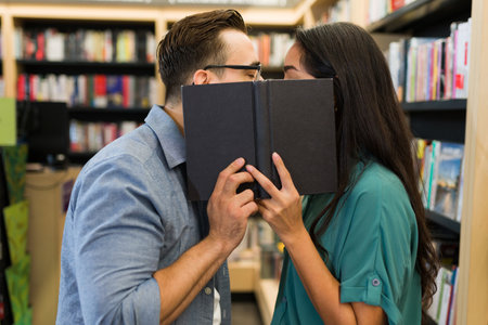 Romantic couple and readers kissing behind a book while shopping at the bookstoreの写真素材