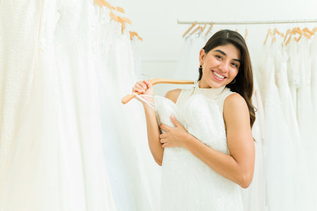 Gorgeous mexican woman looking at the camera smiling while shopping for a beautiful wedding dressの写真素材