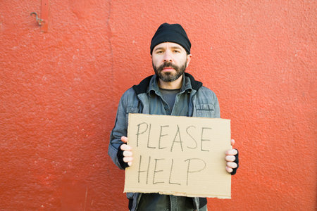 Depressed sad homeless man holding a cardboard sign with please help for money or food