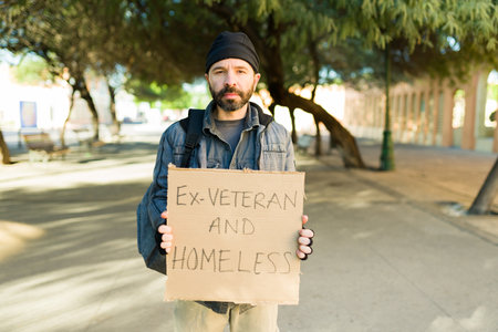 Ex-veteran and homeless man living in poverty in the streets holding a cardboard sign asking for...