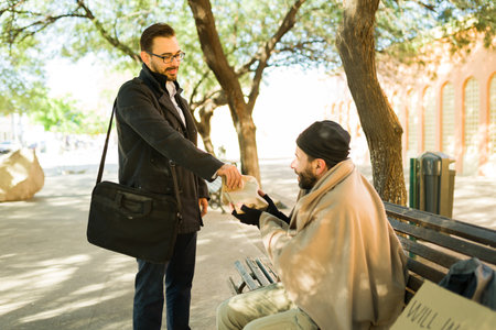 Happy caucasian man spreading kindness and giving food to a hungry miserable homeless manの写真素材