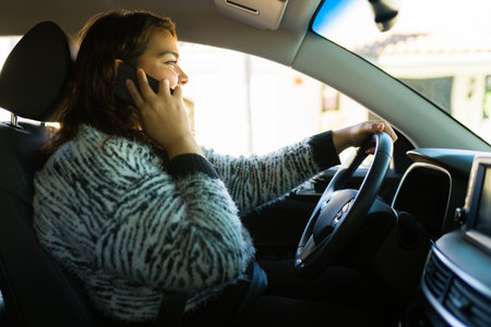 Hispanic big woman behind the wheel driving and smiling while talking on the smart phoneの写真素材