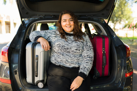 Attractive obese woman ready to travel by car and putting her suitcases on the trunkの写真素材