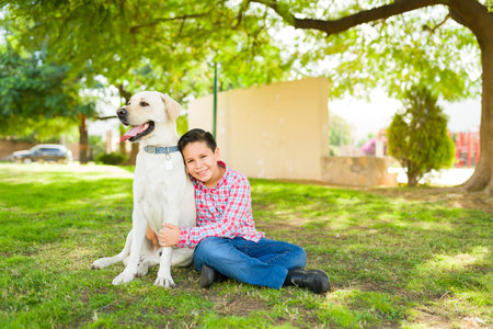 Cheerful hispanic boy hugging his happy retriever dog and smiling while making eye contact and...