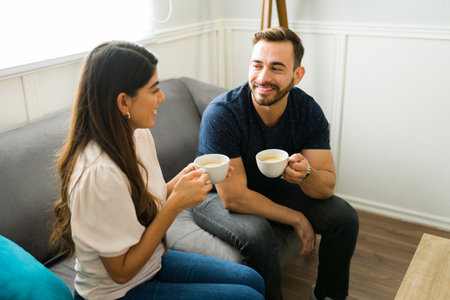 Smiling young couple smiling drinking coffee and talking while relaxing on the sofa