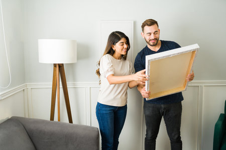 Attractive couple smiling while putting up pictures decorations together at their new homeの写真素材