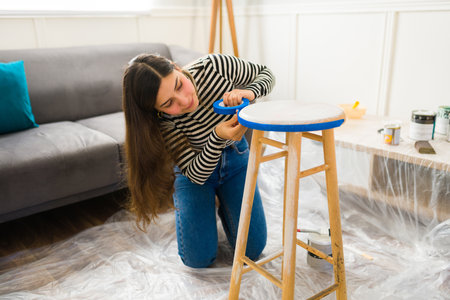 Latin woman doing a furniture flipping project at home and putting scotch paint on a stool to start...