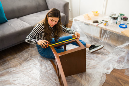 Attractive young woman measuring a chair while working on a furniture flipping project at homeの写真素材