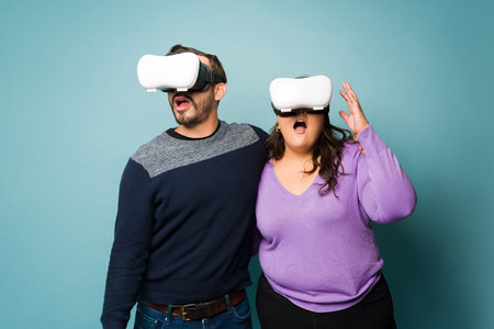 Surprised young couple using VR glasses and looking shocked while playing with virtual reality...