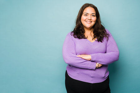 Beautiful mexican obese woman with her arms crossed smiling against a studio background with copy spaceの写真素材