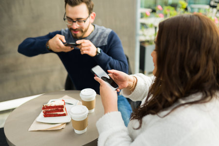 Influencer attractive couple eating at a restaurant cafe and taking pictures with smartphones to the coffee and cake to post on social mediaの写真素材