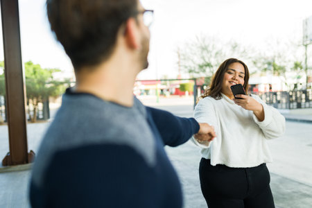 Hispanic fat woman taking a picture with her smartphone for social media while holding hands with her boyfriend during a dateの写真素材