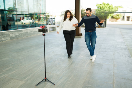 Fun influencer couple dancing with music outdoors in the city while making content for their social...