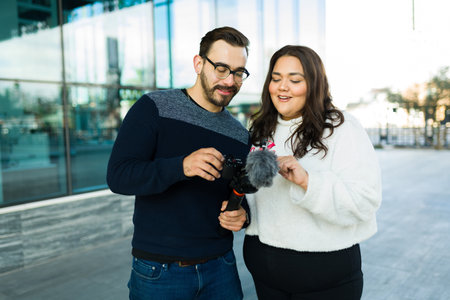 Cheerful woman and man checking a video blog in the city while making content together for social...
