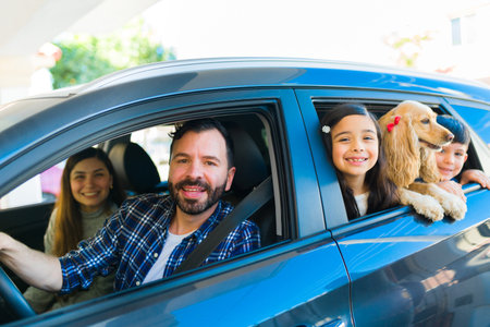 Happy mom and dad driving the car with their little kids and cute family dog while having funの写真素材